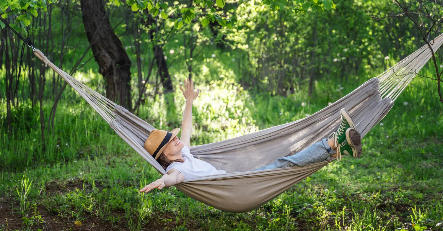 Junge glückliche kaukasische Frau mit Hut liegt in einer Hängematte in einem grünen Garten und genießt einen Sommertag